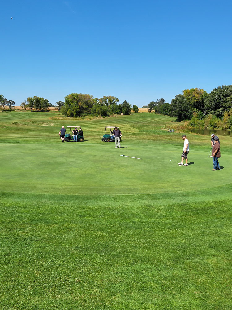 Golfer teeing off with cart at golden hour